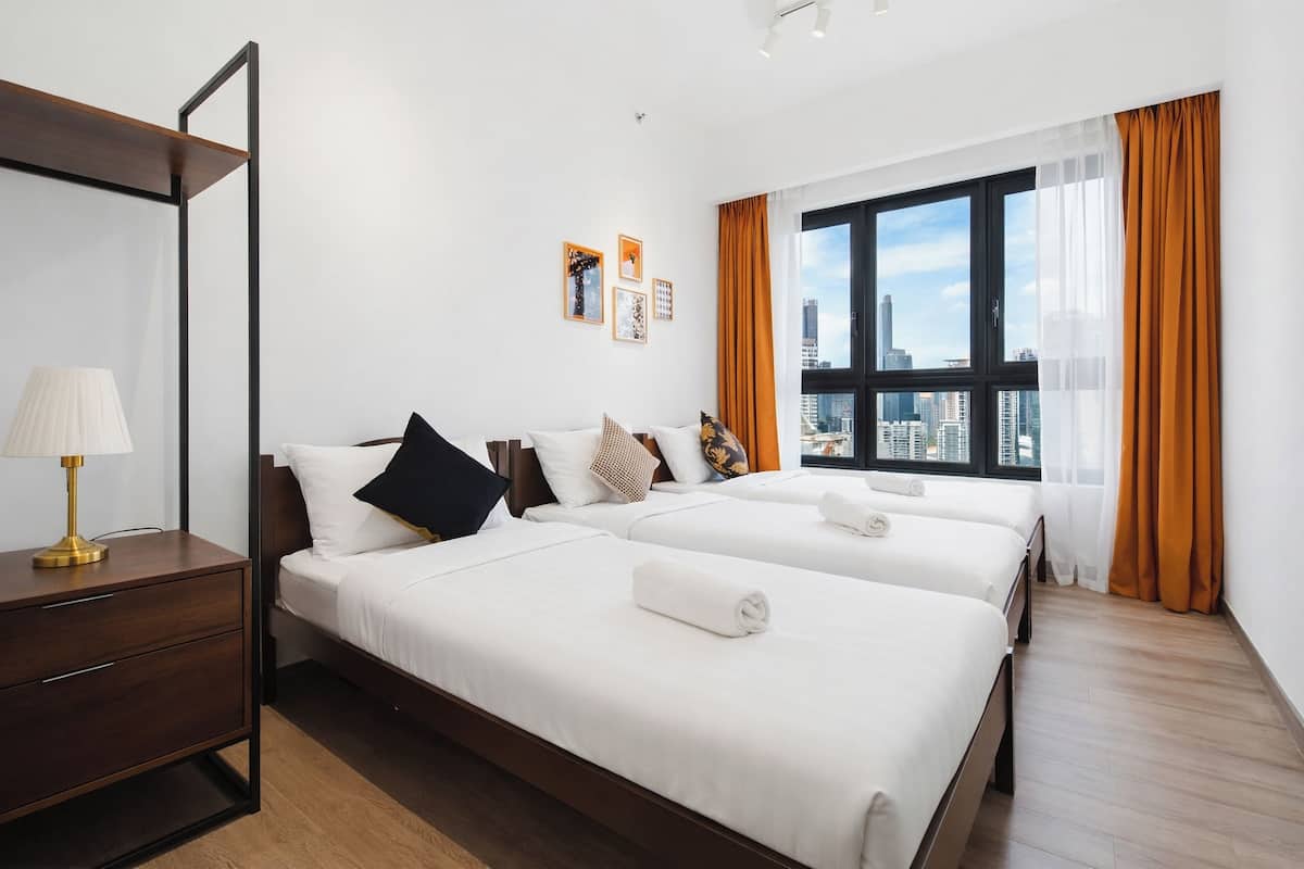 Een hotelkamer met twee bedden, een nachtkastje, een lamp en een groot raam met gordijnen.