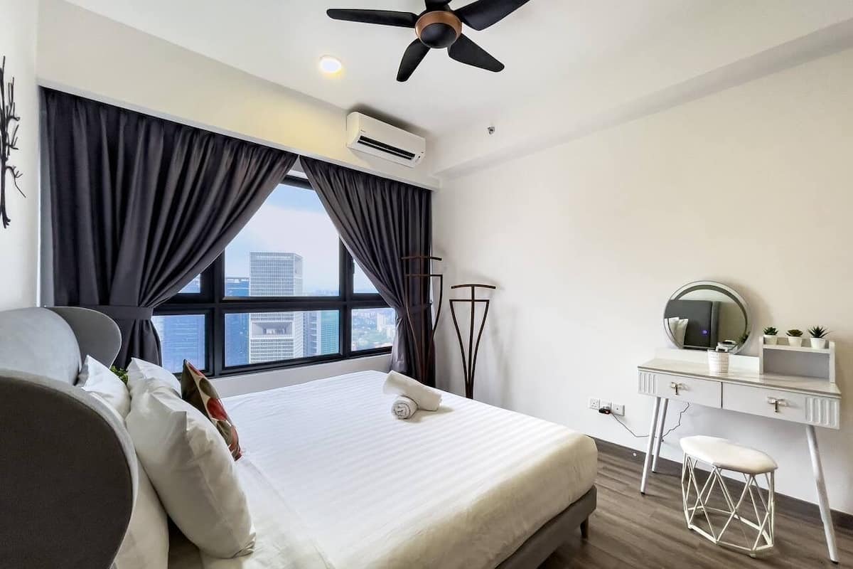 A modern hotel room with a large bed, a desk with a mirror, and a view of the city.