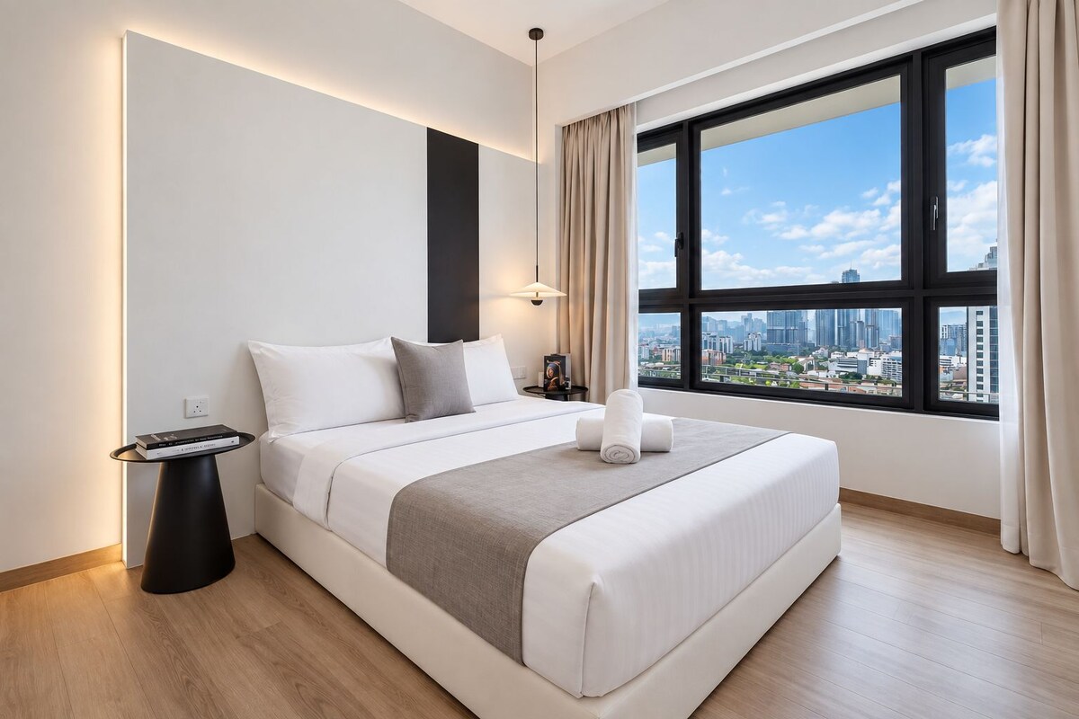 Habitación de hotel moderna con una cama grande, una mesita de noche, una lámpara y una ventana con vistas a la ciudad.