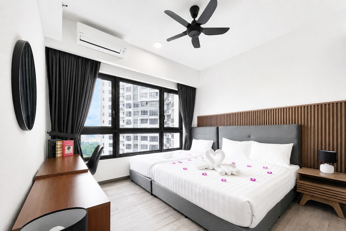 A modern hotel room with a large bed, a desk, a chair, a ceiling fan, and a view of the city through large windows.