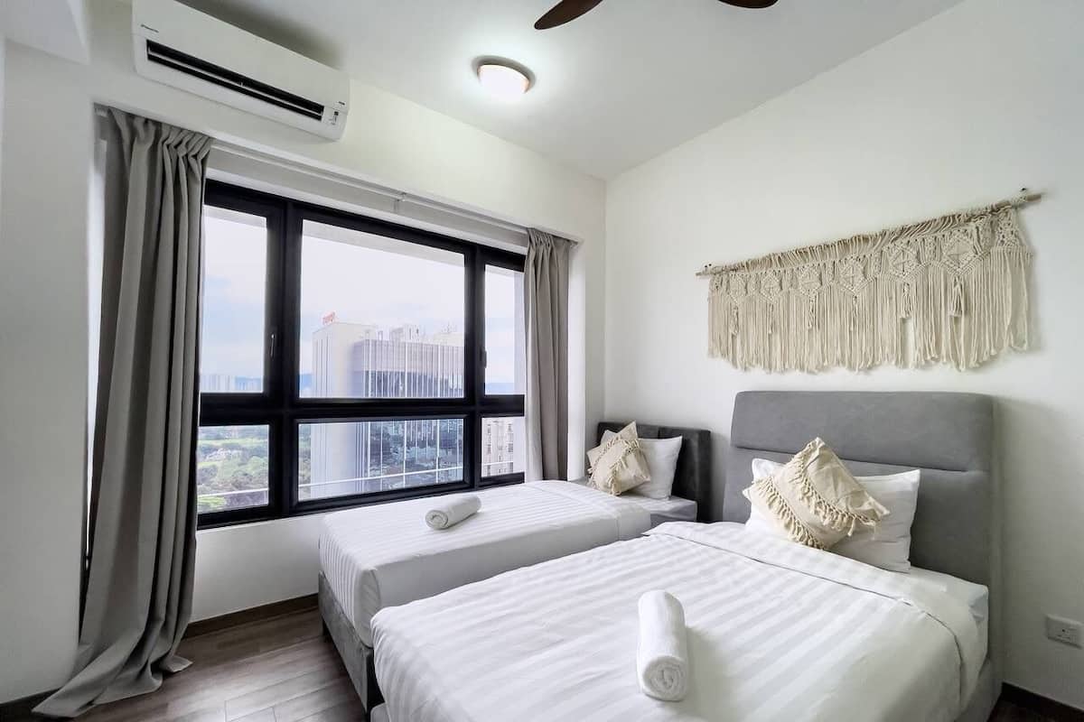 A hotel room with two beds, a large window with curtains, a ceiling fan, and a macrame wall hanging.