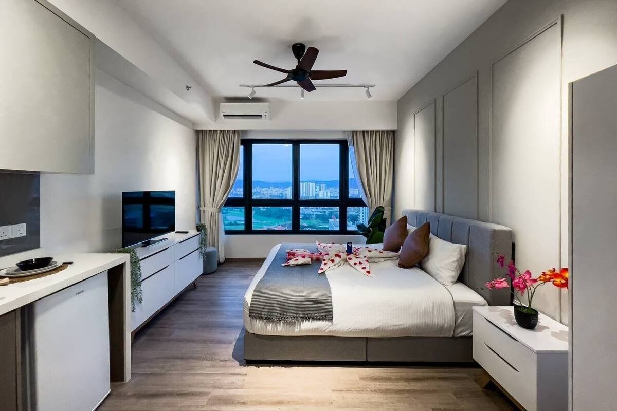 A modern bedroom with a large bed, a TV, and a view of the city.
