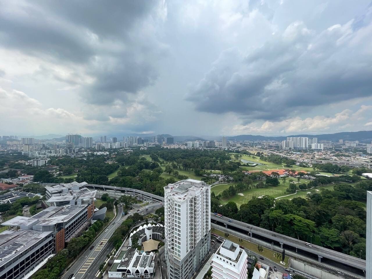 A high-rise building with a modern architectural design, surrounded by a cityscape with various buildings and a green park area.