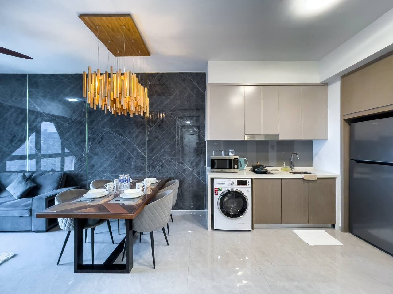 A modern kitchen with a built-in washer, a dining area with a wooden table, and a grey sofa.
