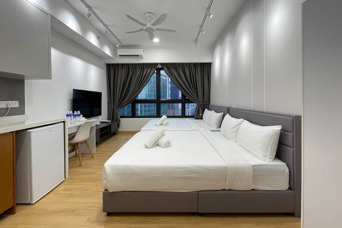 A modern hotel room with a large bed, a desk, a television, and a view of the city through the window.