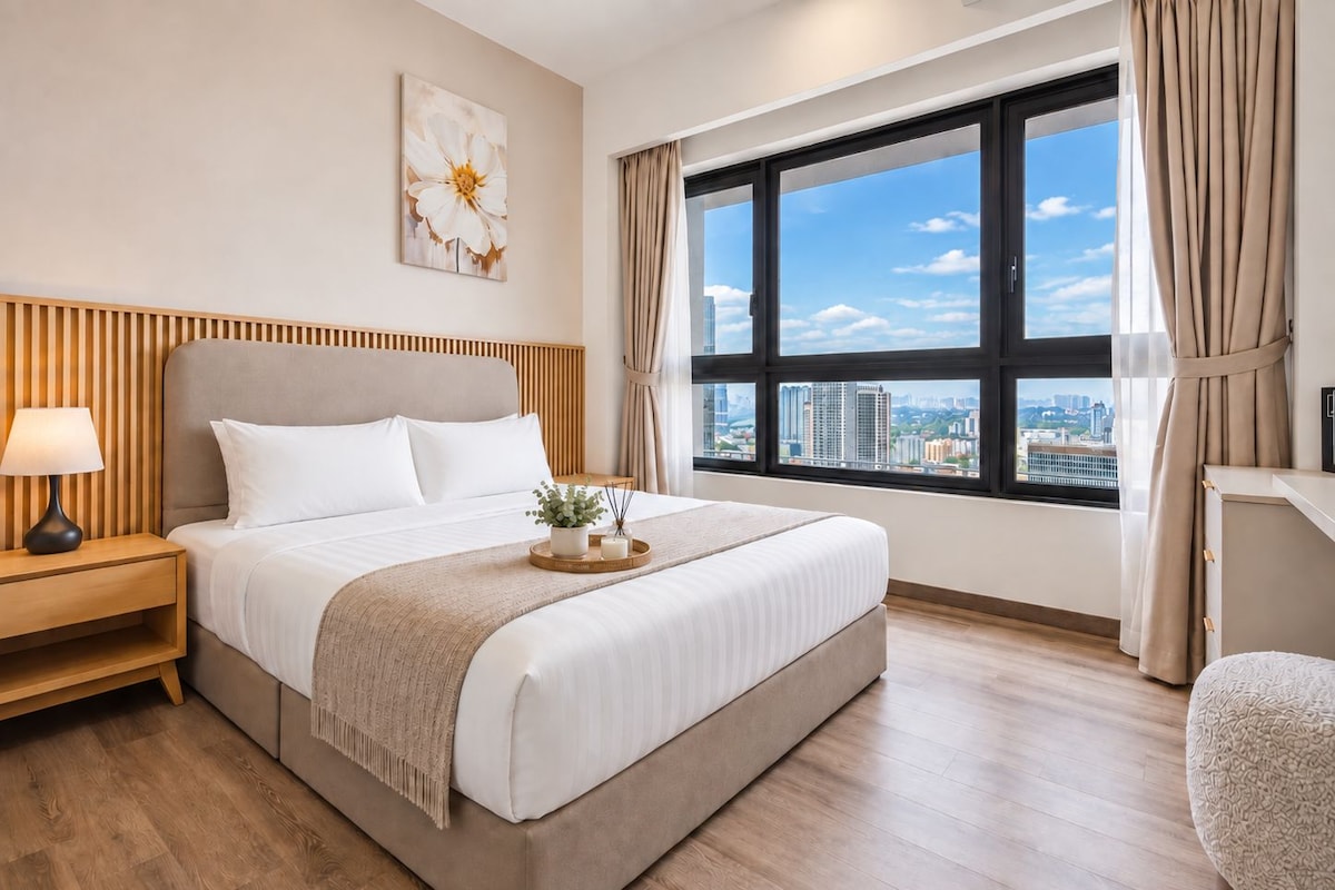 A hotel room with a large bed, a nightstand, a window with a city view, and a decorative wall piece.