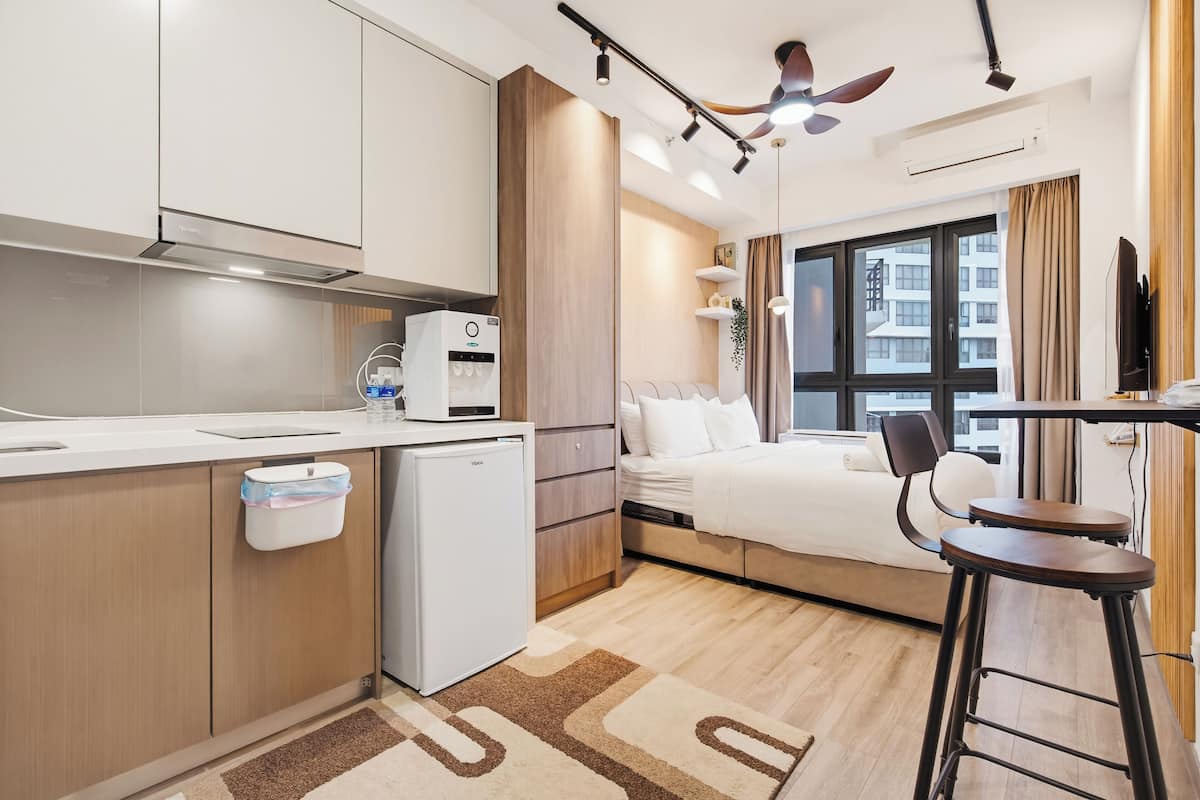 A modern hotel room with a kitchenette, a bed, a desk, and a view of the city.