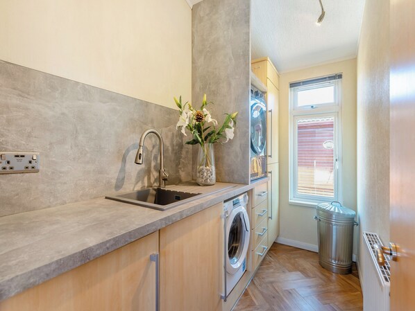A modern kitchen with a built-in washing machine, a sink with a faucet, and a window with blinds.