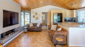 A modern living room with a large flat-screen TV, two sofas, a coffee table, and a herringbone-patterned wooden floor.