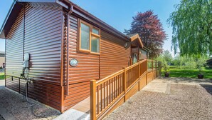 A wooden cabin with a balcony, a satellite dish, and a gravel driveway.