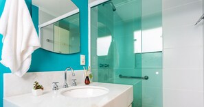 A bathroom with a white sink, a mirror, a glass shower enclosure, and a teal wall.