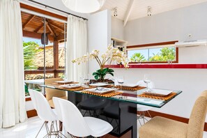 Un comedor con mesa de vidrio, sillas blancas y vistas al exterior.