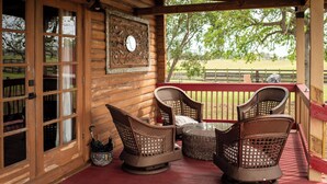 A wooden porch with wicker chairs and a table, overlooking a fenced yard. - Peaceful Farm Cabin Getaway, 2BR w/ WiFi, AC & Sunrise Views (Okeechobee)