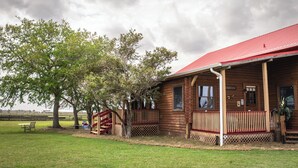 A wooden cabin with a red roof, a porch, and a fenced yard. - Peaceful Farm Cabin Getaway, 2BR w/ WiFi, AC & Sunrise Views (Okeechobee)