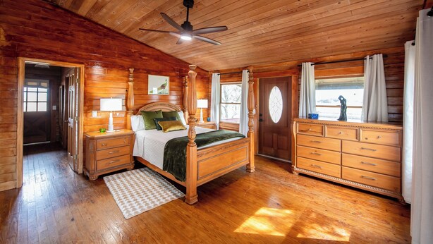 A wooden cabin bedroom with a four-poster bed, a nightstand, a dresser, and a ceiling fan. - Peaceful Farm Cabin Getaway, 2BR w/ WiFi, AC & Sunrise Views (Okeechobee)