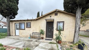 A single-story house with a front door, a bench, and potted plants.