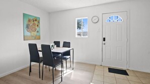 A dining area with a table and chairs, a clock, a door, and a window.