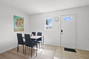 Un comedor con una mesa, sillas, un reloj, una puerta y una ventana.