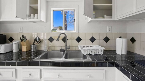 A kitchen with a double sink, white cabinets, a window with a view, and a tiled backsplash.