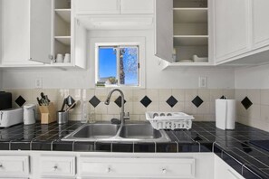 A kitchen with a double sink, white cabinets, a window with a view, and a tiled backsplash.