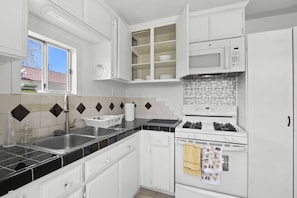 A kitchen with white cabinets, a stove, a microwave, and a window.