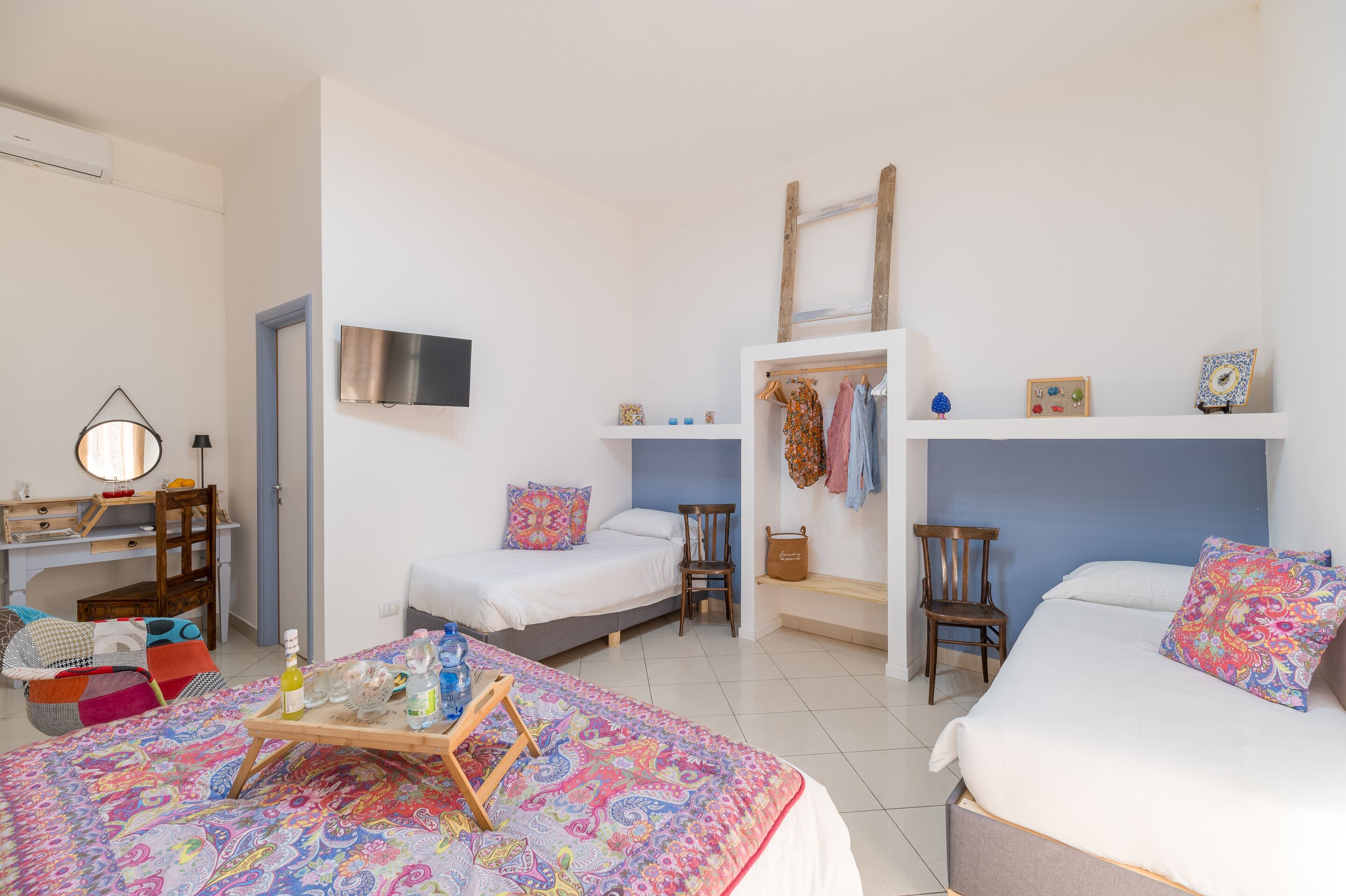A bedroom with two beds, a desk, a chair, a wardrobe, and a TV.