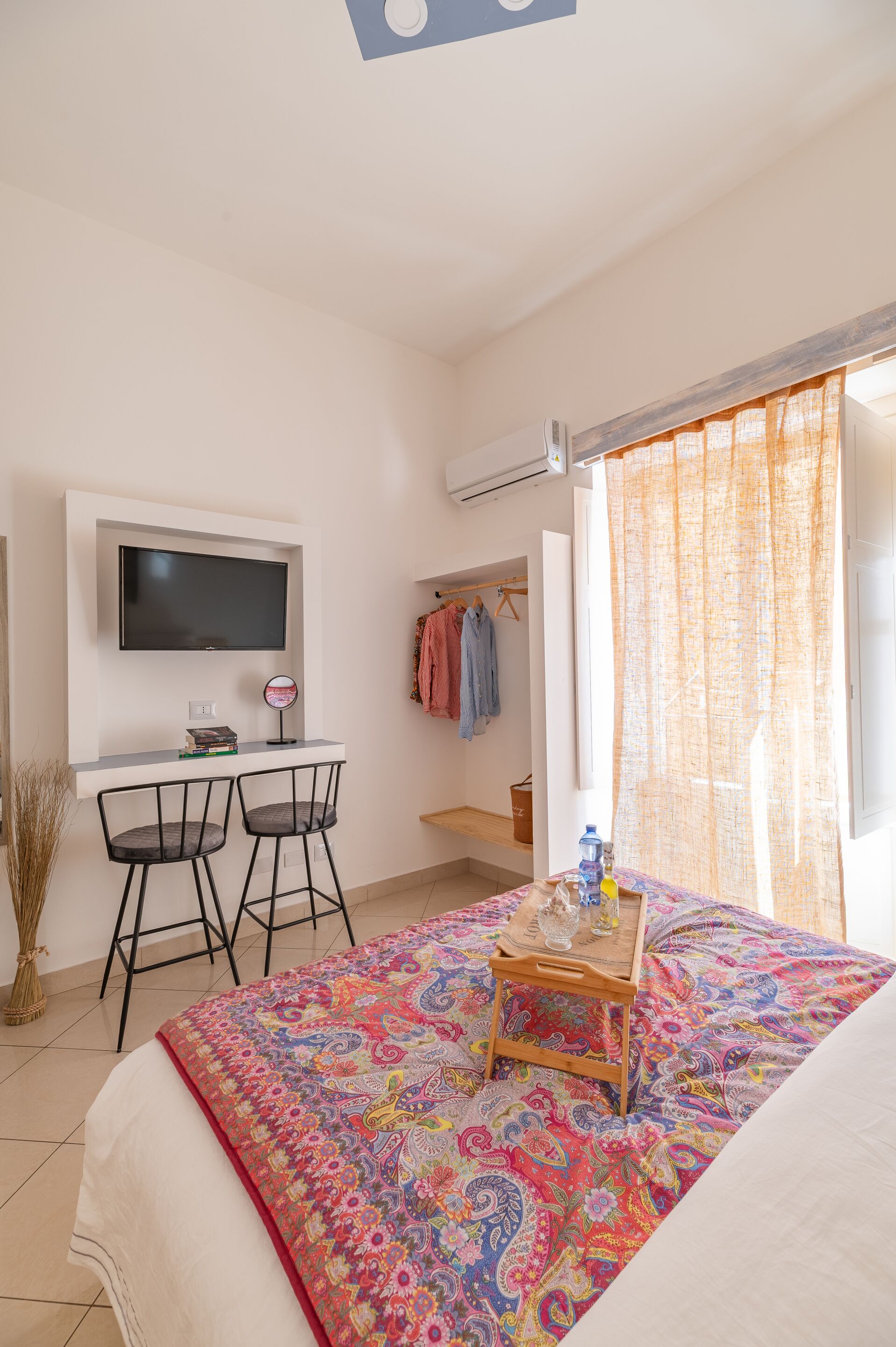 Un dormitorio con una cama, un escritorio y dos sillas, un televisor y una ventana con cortinas.