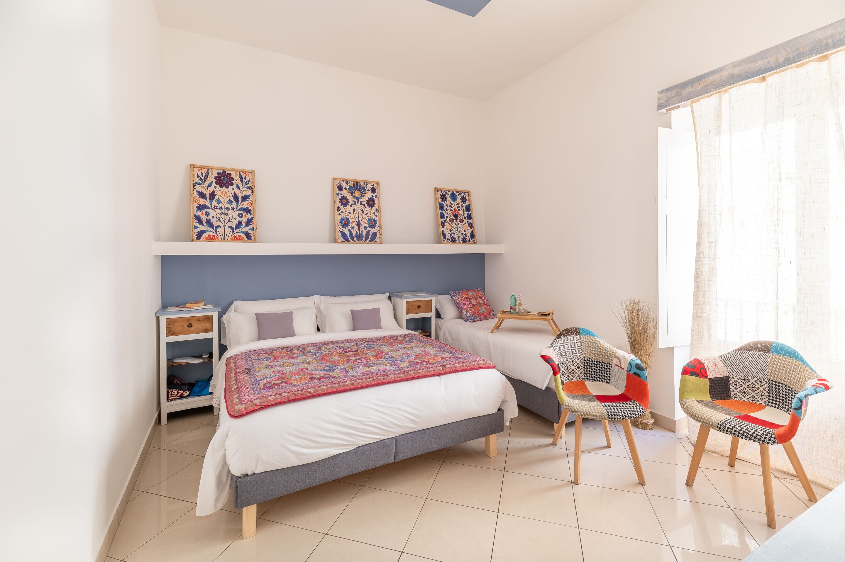 A bedroom with a bed, two nightstands, a chair, and a window with curtains.