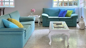 A living room with two teal sofas, a white coffee table, and a wall-mounted light.