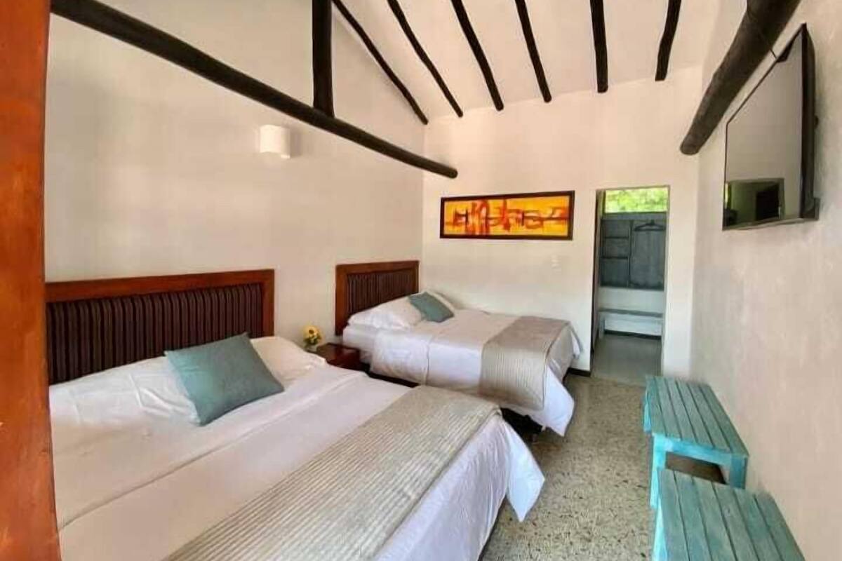 A room with two beds, a bench, and a painting on the wall.