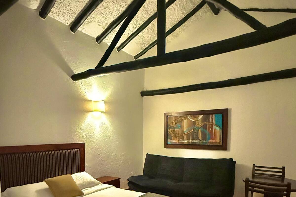A bedroom with a bed, a chair, a sofa, and a painting on the wall.