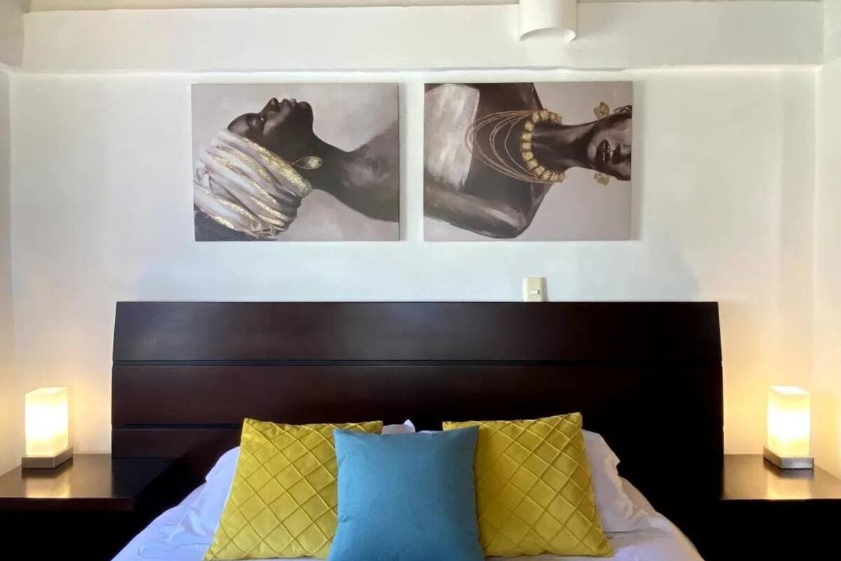 A bedroom with a bed, two wall-mounted paintings, and bedside lamps.