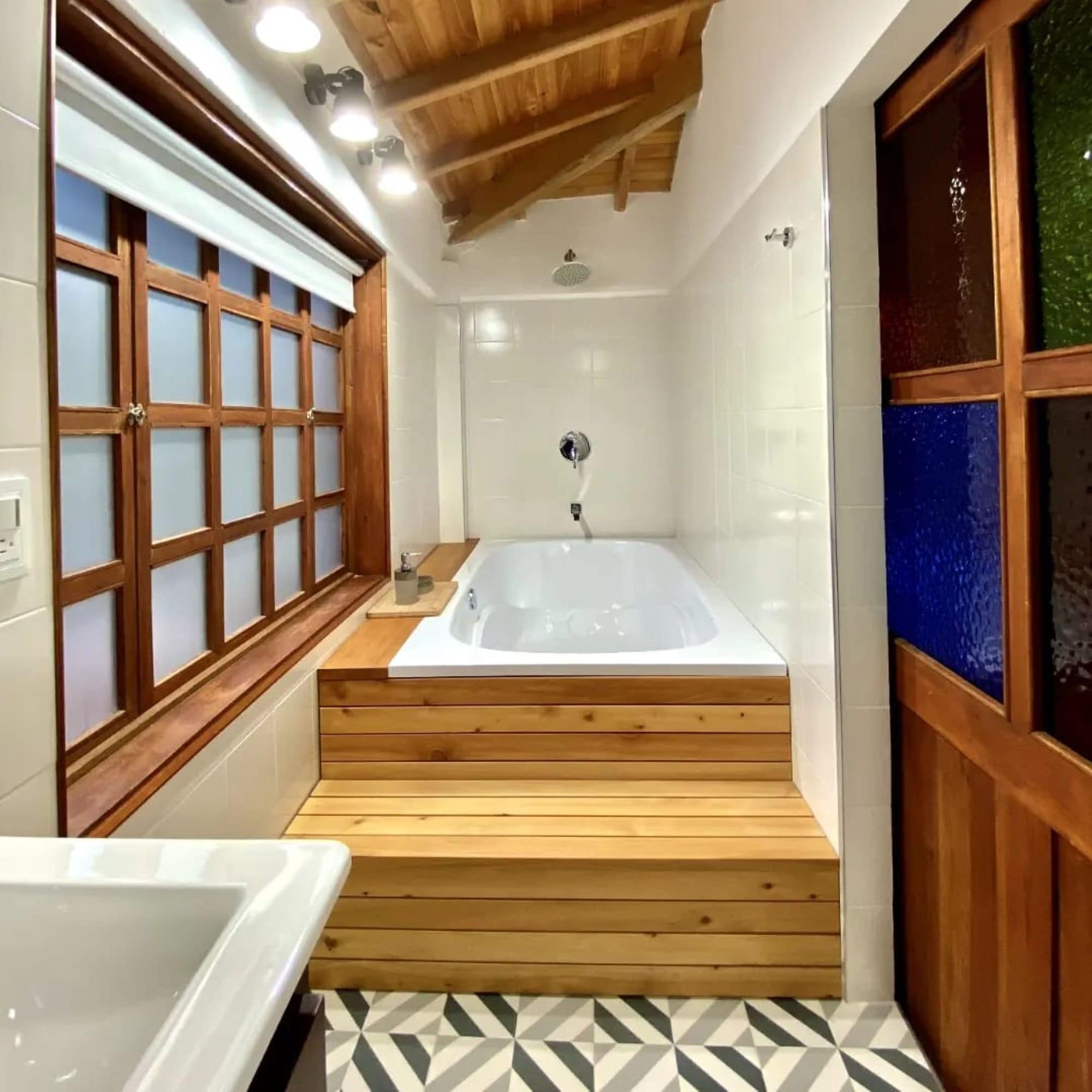 A bathroom with a wooden bathtub, a shower, and a window with frosted glass.
