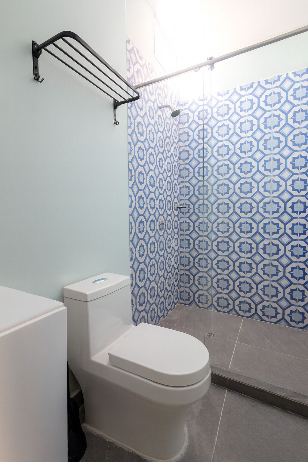A bathroom with a white toilet, a shower with blue patterned tiles, and a metal towel rack.
