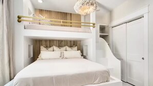 A modern bedroom with a bunk bed, a chandelier, and a white wardrobe.
