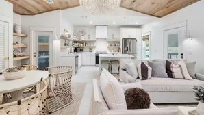 A modern kitchen with white cabinets, a stainless steel refrigerator, and a dining area with a round table and wicker chairs.