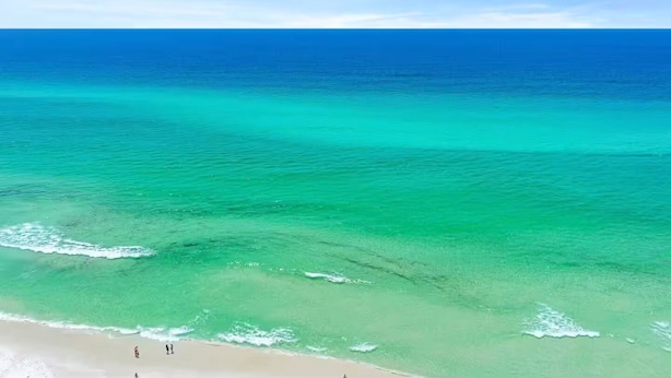 A beach with clear turquoise waters and a few people walking along the shore.