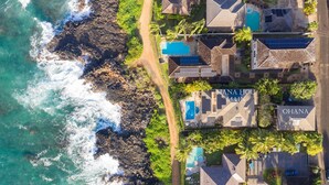 An aerial view of a coastal property with a swimming pool, solar panels, and a clear view of the ocean.