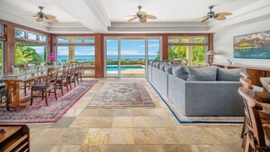 A spacious living area with a large sofa, dining table, and chairs, a view of the ocean, and ceiling fans.