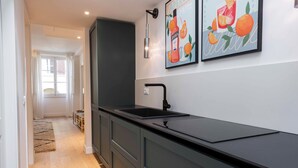 Een moderne keuken met donkere kastjes, een zwart aanrechtblad en een spoelbak. Twee ingelijste foto's hangen aan de muur, en er ligt een vloerkleed.