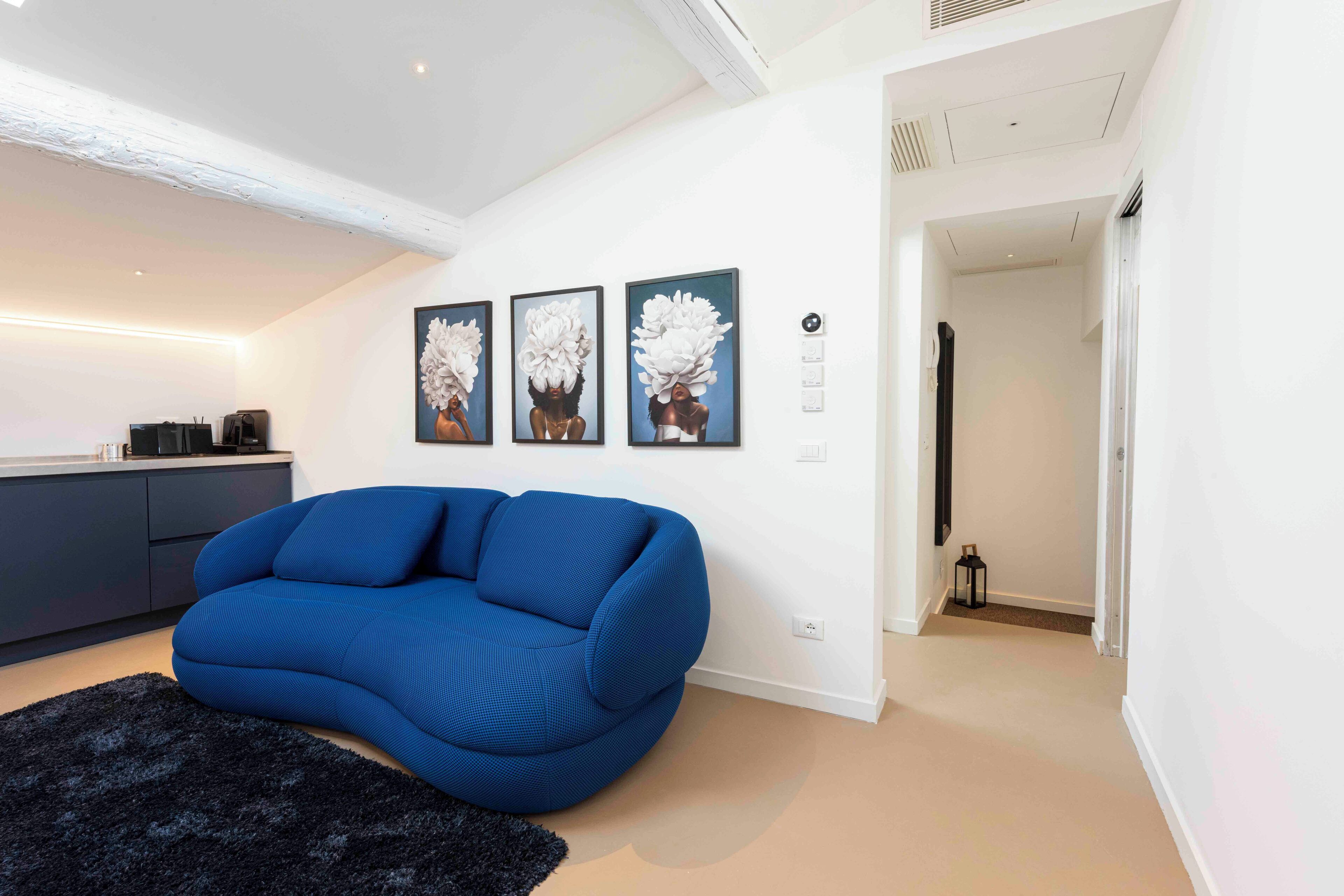 Uma sala de estar moderna com um sofá azul, um tapete preto e três quadros de flores pendurados na parede.