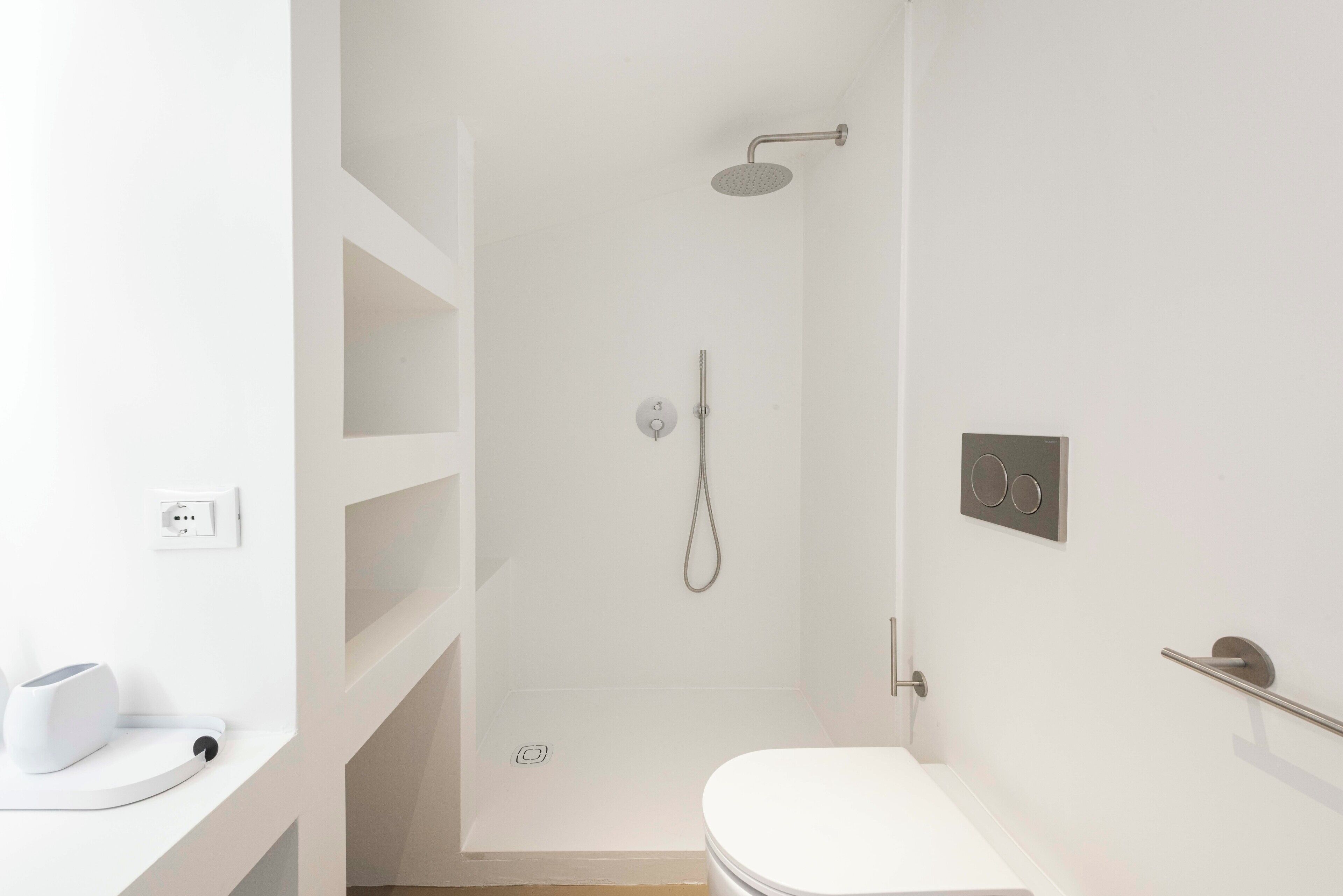 A modern bathroom with a shower, toilet, and a white countertop with a device.