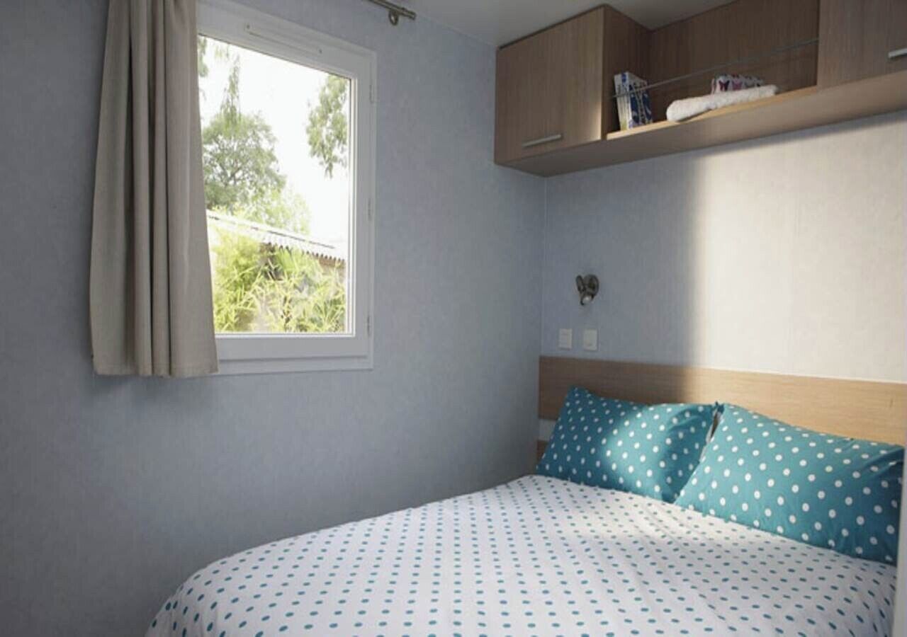 A bedroom with a bed, a window, and a wooden shelf above the bed.