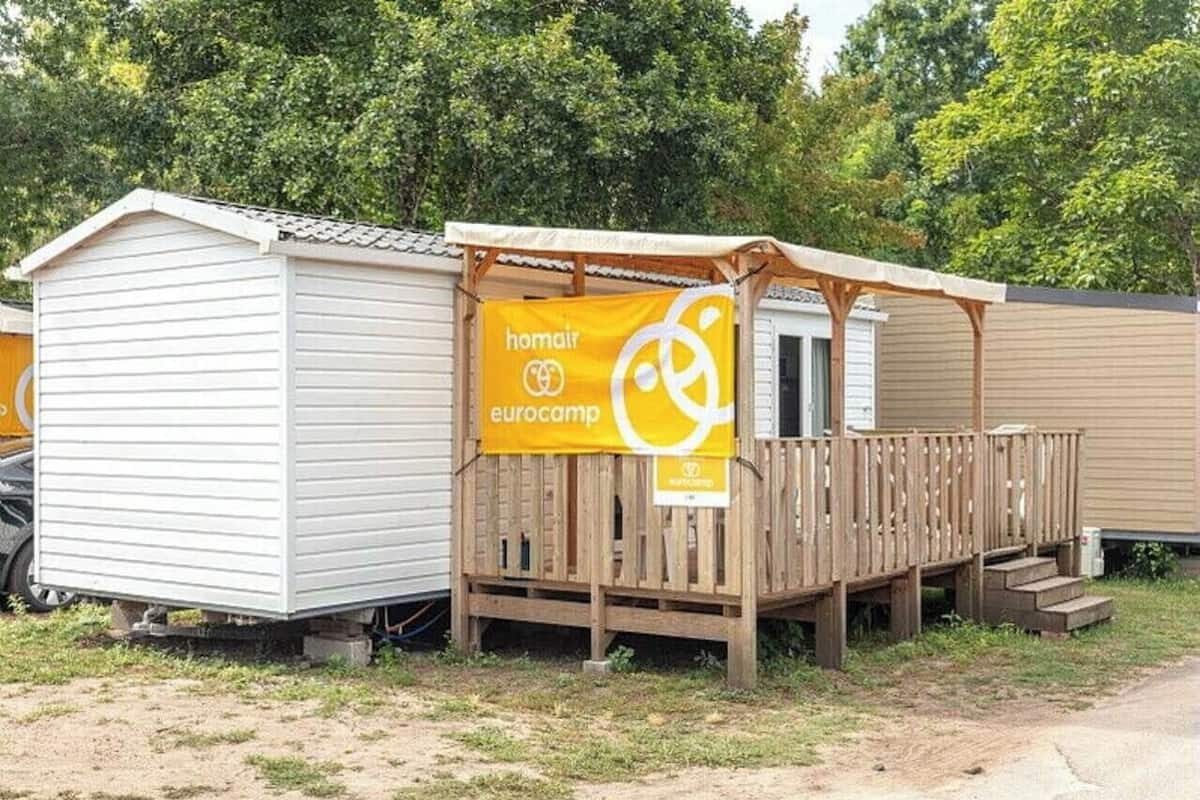 Une maison mobile dotée d’une terrasse en bois et d’une enseigne indiquant « homair eurocamp ».