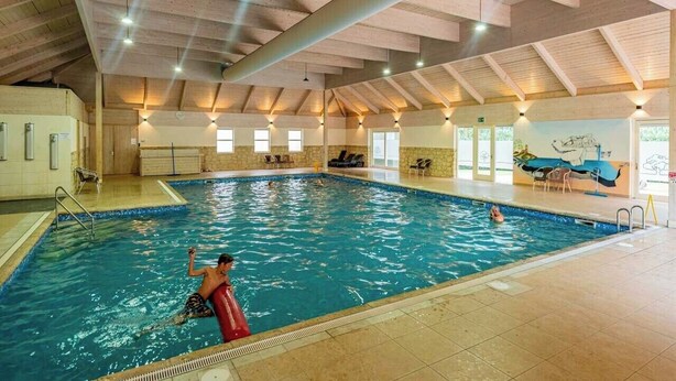 Une piscine intérieure avec des poutres en bois au plafond, un poste de surveillance pour le sauveteur et une fresque murale.