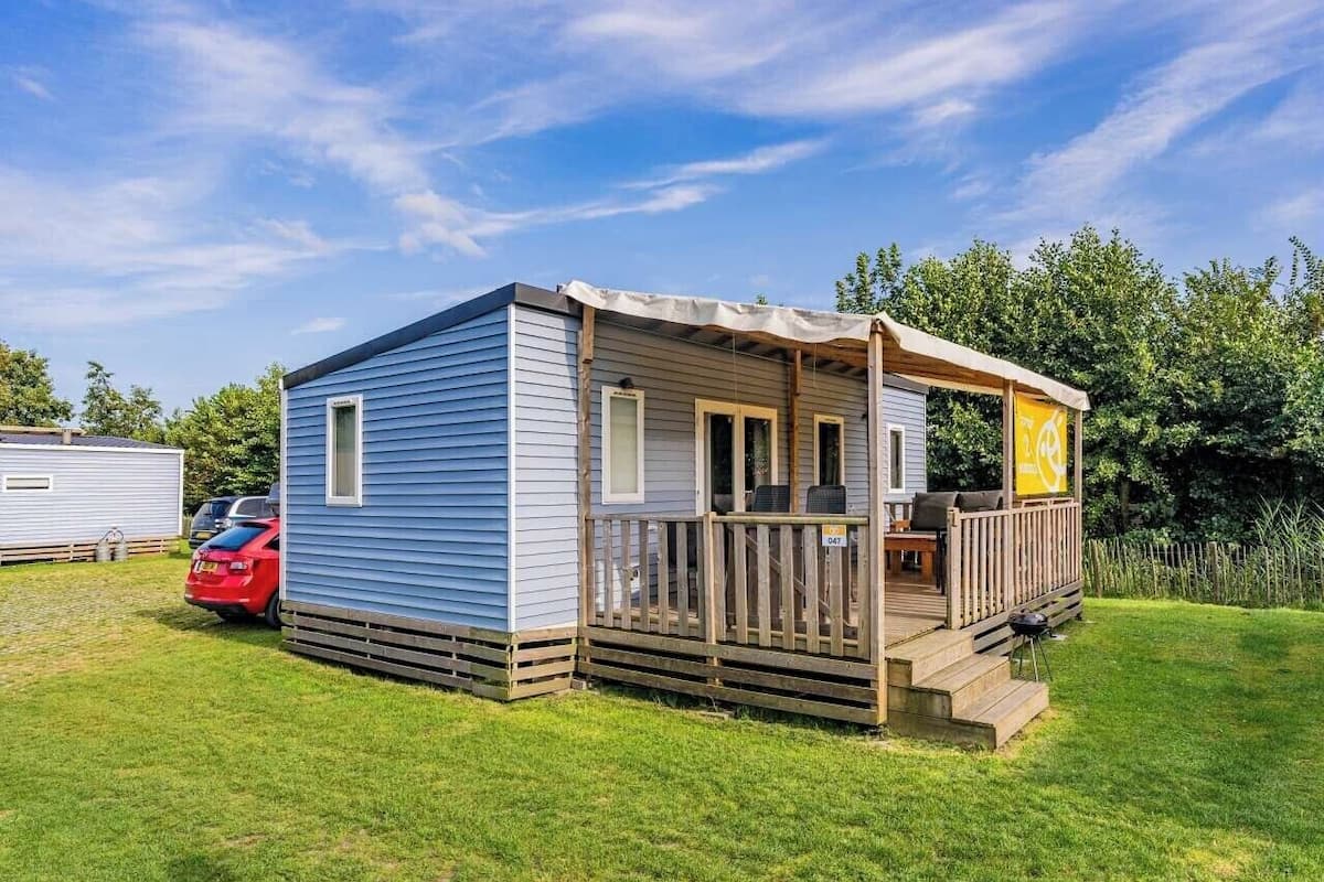 Une maison mobile dotée d’une véranda, d’une petite terrasse et d’une voiture garée à proximité.