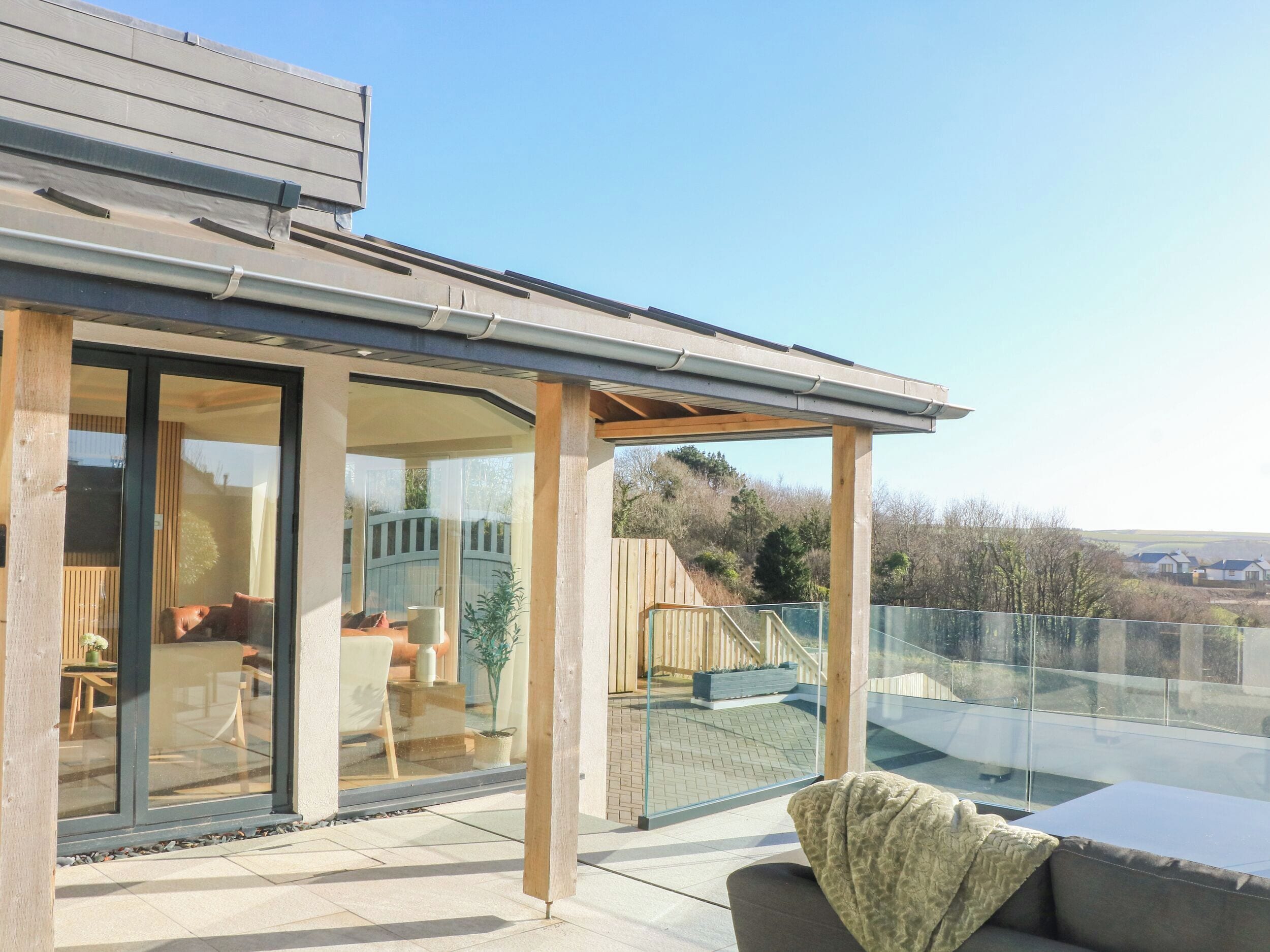 A modern house with a glass-enclosed patio, a wooden deck, and a view of the surrounding landscape.