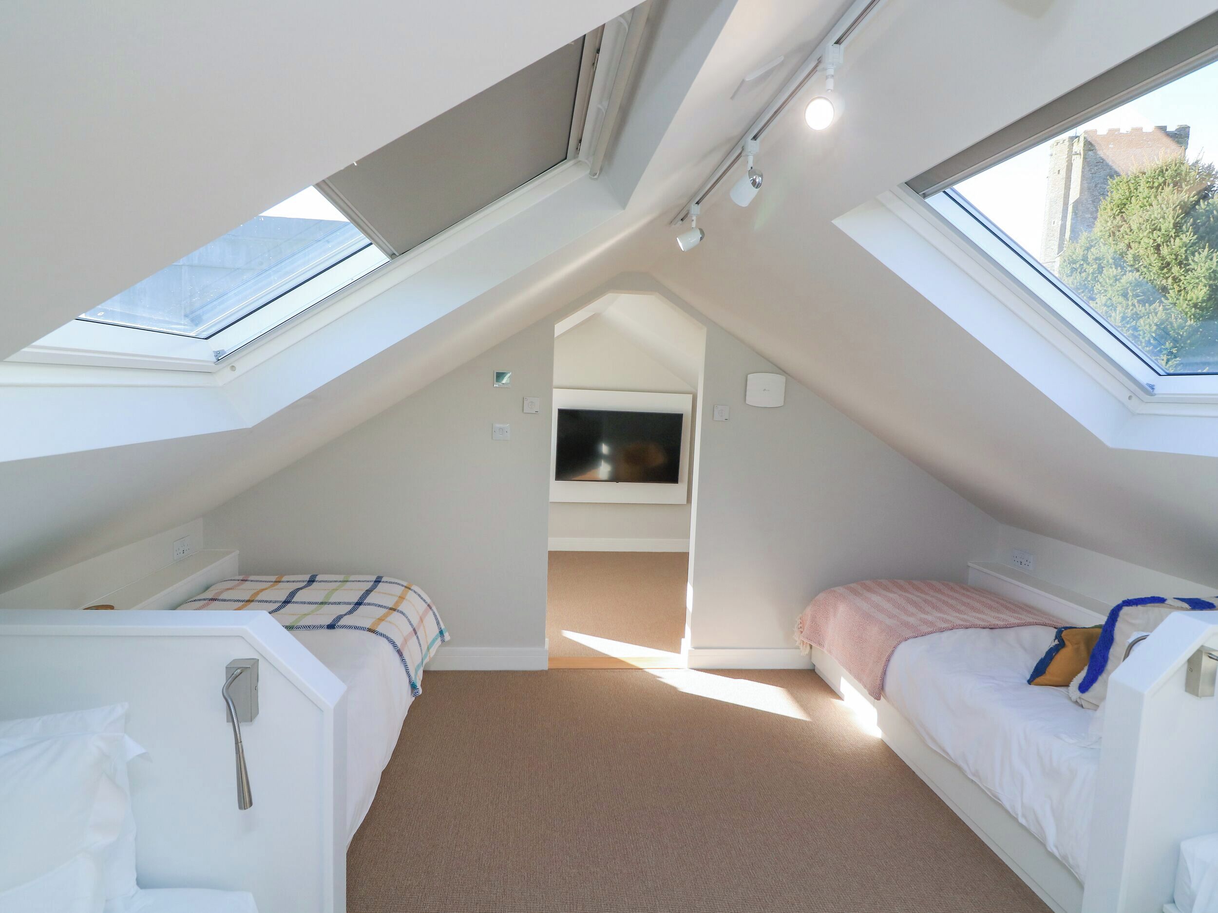 Ein kleines, helles Schlafzimmer im Dachgeschoss mit zwei Betten, einem Fernseher und Dachfenstern.