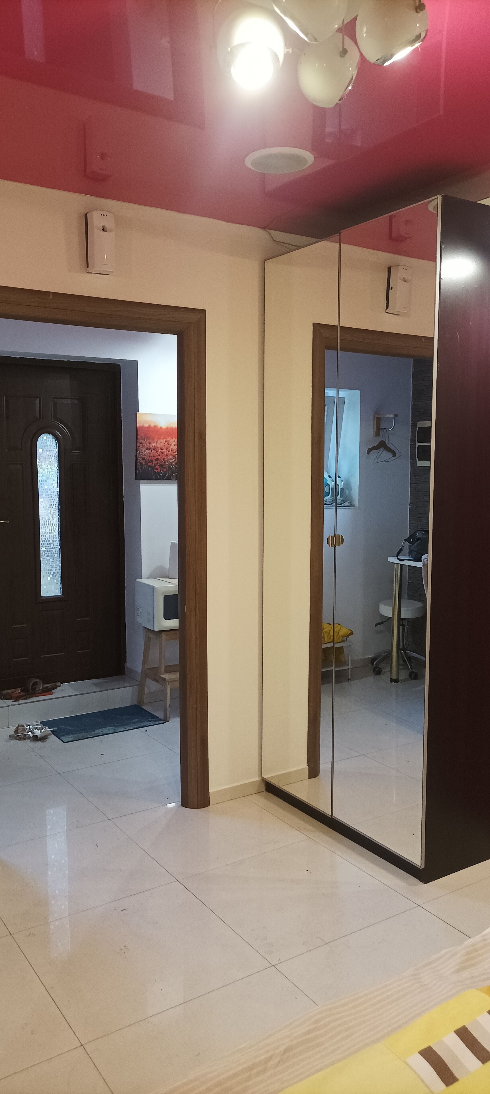 Una habitación con un espejo grande, una puerta con ventanal, una mesita y una silla.