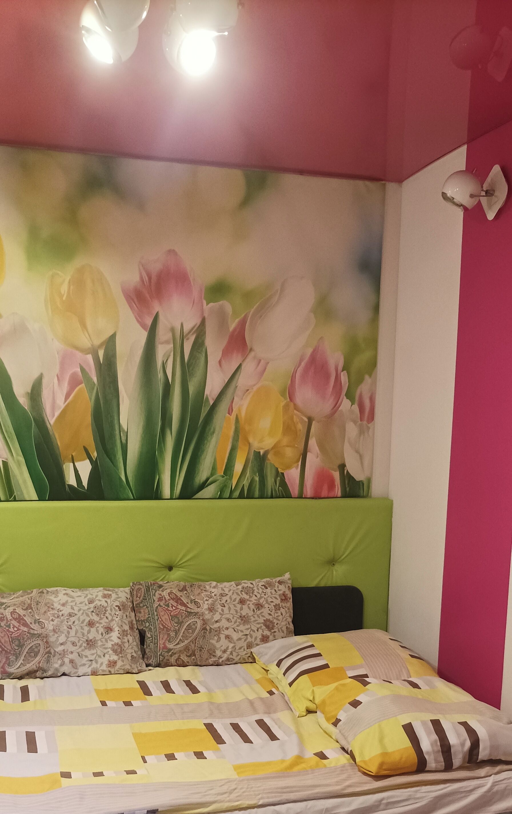 Quarto com cama, cabeceira verde, arte floral na parede e parede rosa.